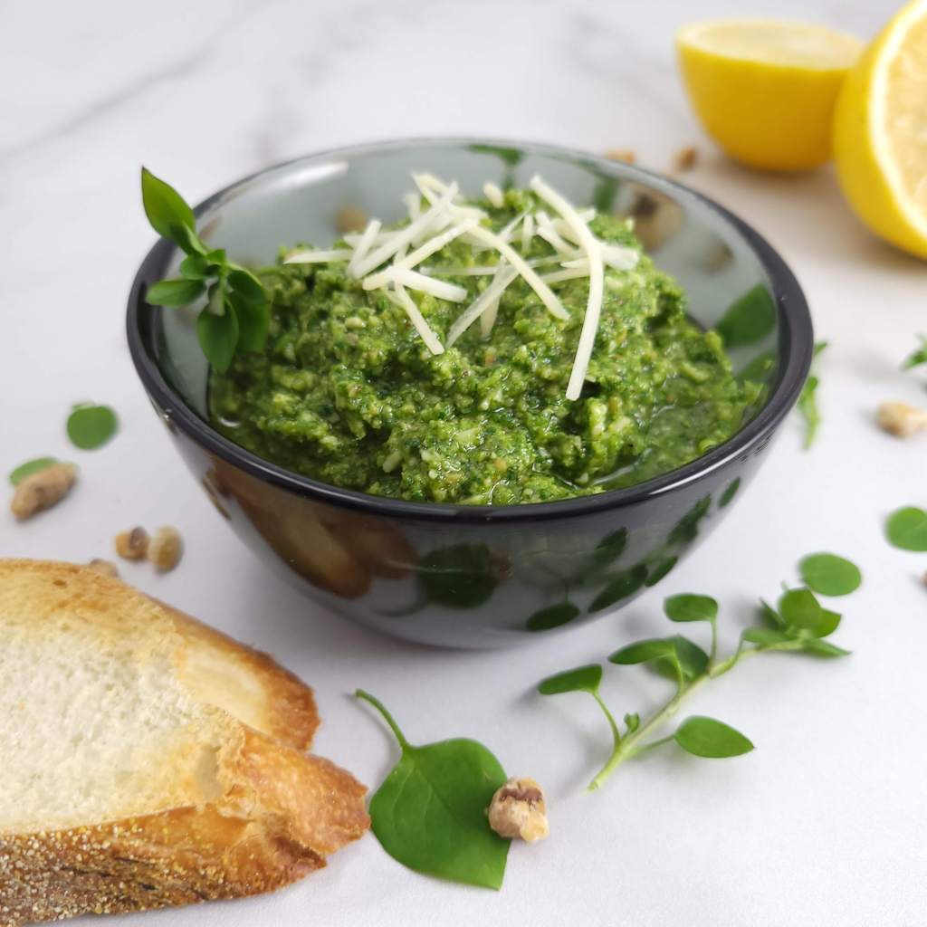 A bowl of chickweed pesto with toast and lemon halves 